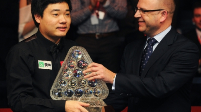 Dings Junhui saņem "Masters" trofeju no turnīra galvenā sponsora "Ladbrokes" pārstāvja Gerija Makilraita rokām.
Foto: AFP/Scanpix