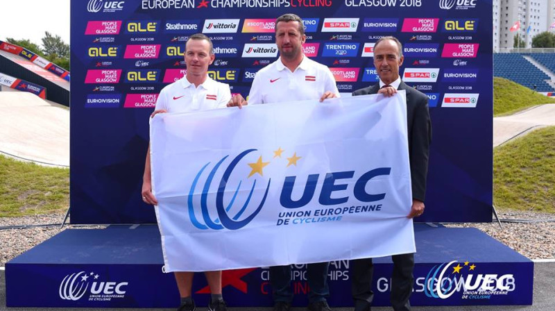 BMX izlases mendžeris Arits Ozols (no kreisās) un Ivo Lakučs saņem UEC Eiropas kausa karogu no UEC prezidenta Roko Kataneo.

Foto: UEC.ch