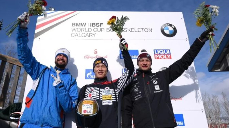 Tomass Dukurs blakus olimpiskajiem čempioniem uz goda pjedestāla Kalgari. Foto: IBSF