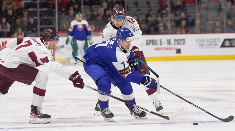 Latvijas U20 valstsvienības hokejisti Roberts Cjunskis (Nr. 12) un Rainers Rullers (Nr. 7) cīņā pret Slovākijas komandas kapteini Simonu Ņemecu. Foto: Ron Ward/AP/Scanpix